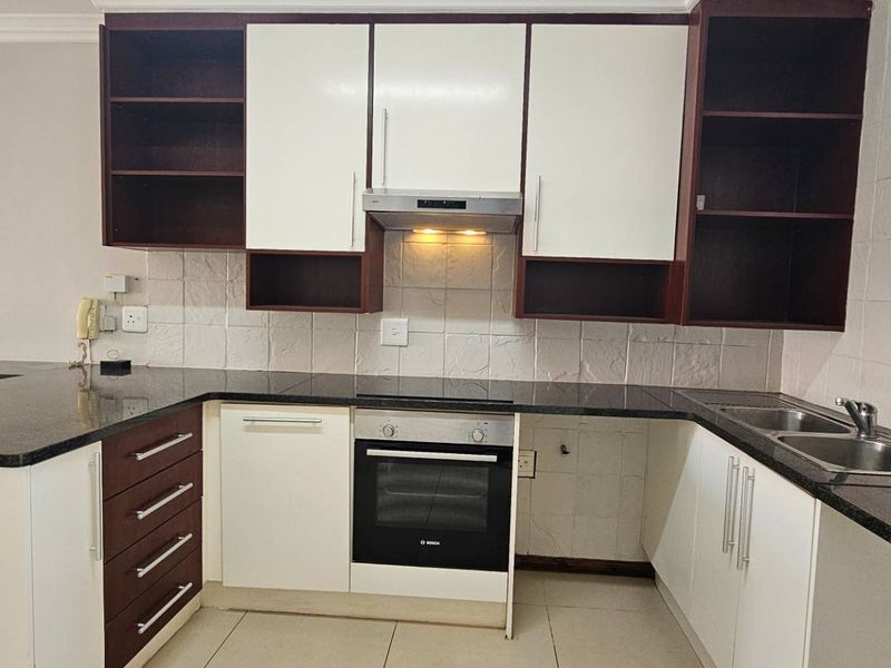 A clean and functional kitchen featuring dark granite countertops, built-in oven, extractor fan, and ample storage cabinetry with a neutral tiled backsplash.
