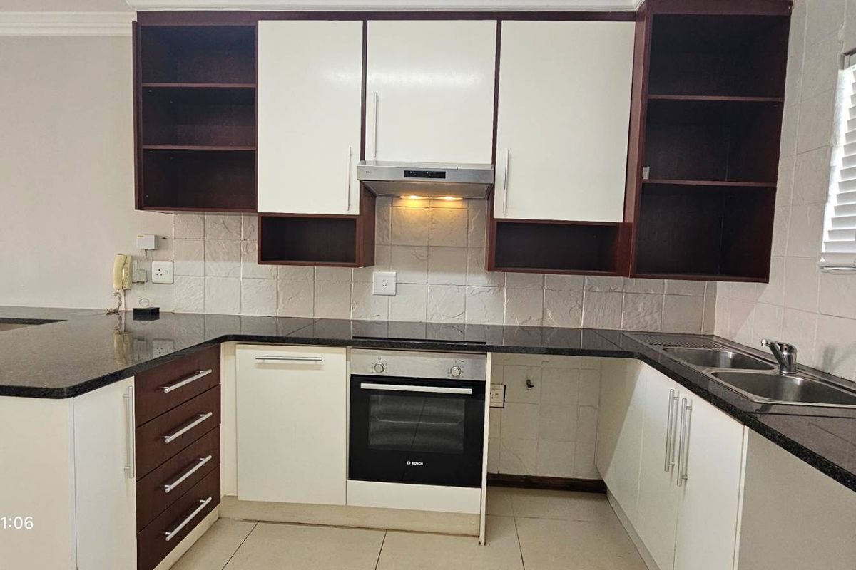 A clean and functional kitchen featuring dark granite countertops, built-in oven, extractor fan, and ample storage cabinetry with a neutral tiled backsplash.
