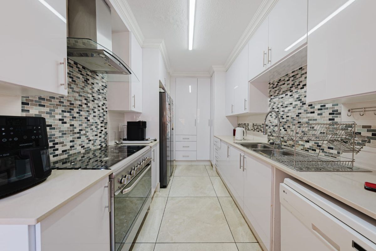 Modern galley-style kitchen featuring white cabinetry, mosaic tile backsplash, stainless steel appliances, and tiled flooring with ample storage space.