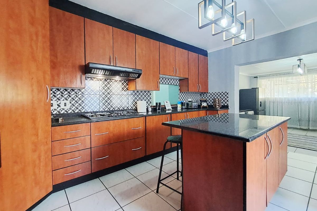 A well-maintained kitchen featuring warm-toned wooden cabinetry, granite countertops, a central island, and a stylish patterned tile backsplash.