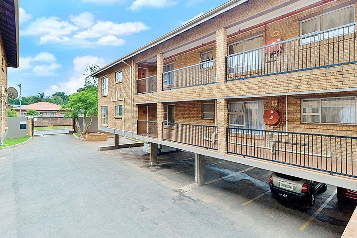 Exterior view of a multi-story townhouse complex featuring face-brick facade, covered balcony walkways, and ground-level under-cover parking bays.