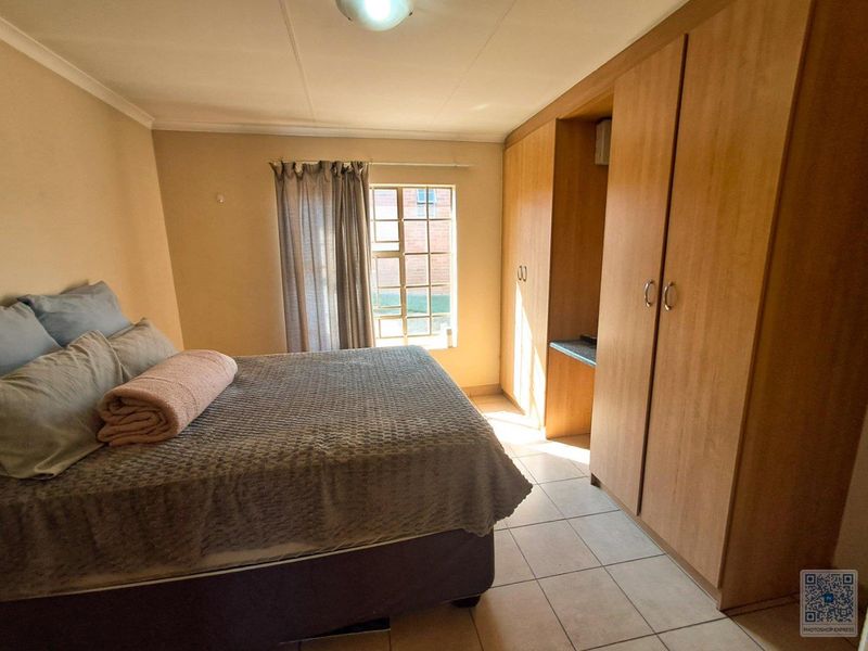 A functional bedroom featuring built-in wooden cupboards, tiled flooring, and natural light from a window.