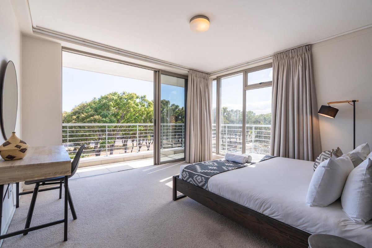 Bright bedroom featuring large sliding glass doors opening onto a private balcony with scenic views and neutral carpeted flooring.