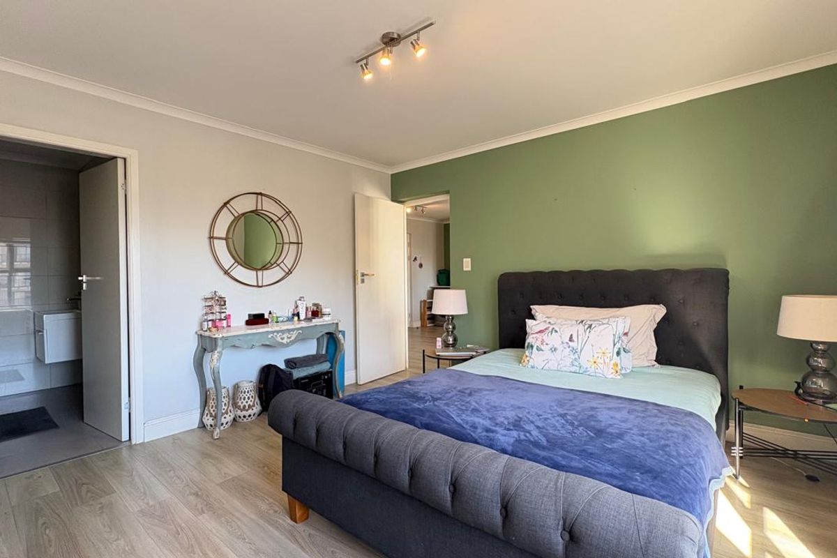 A well-maintained bedroom featuring laminate flooring, a green accent wall, and an en-suite bathroom entrance.
