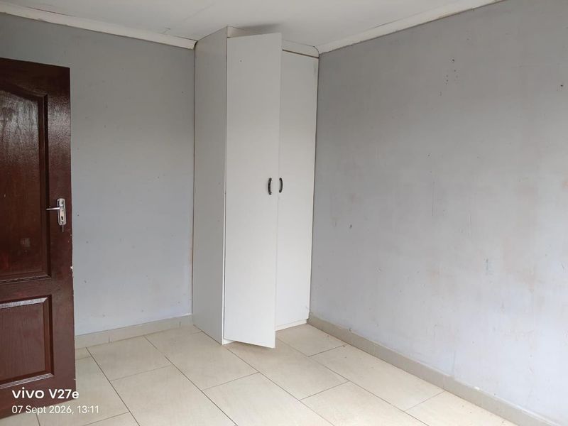 A simple, empty bedroom featuring tiled flooring and a built-in white wardrobe, requiring minor cosmetic updates to the wall finishes.