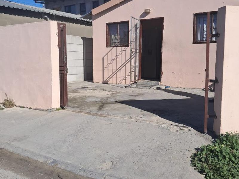 Front exterior view of a single-story house featuring a concrete driveway, boundary wall, and metal security gate.