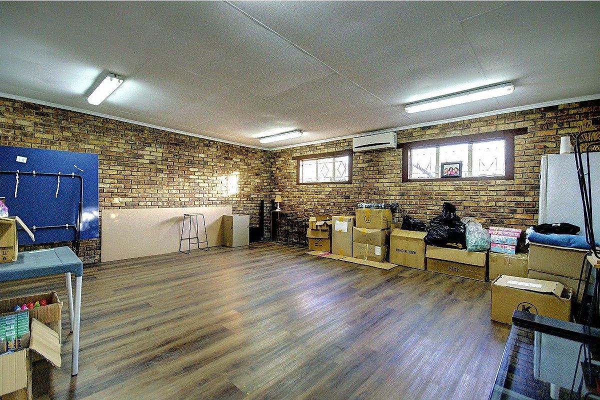 A spacious multi-purpose room featuring exposed brick walls, wood-look flooring, and a wall-mounted air conditioning unit.