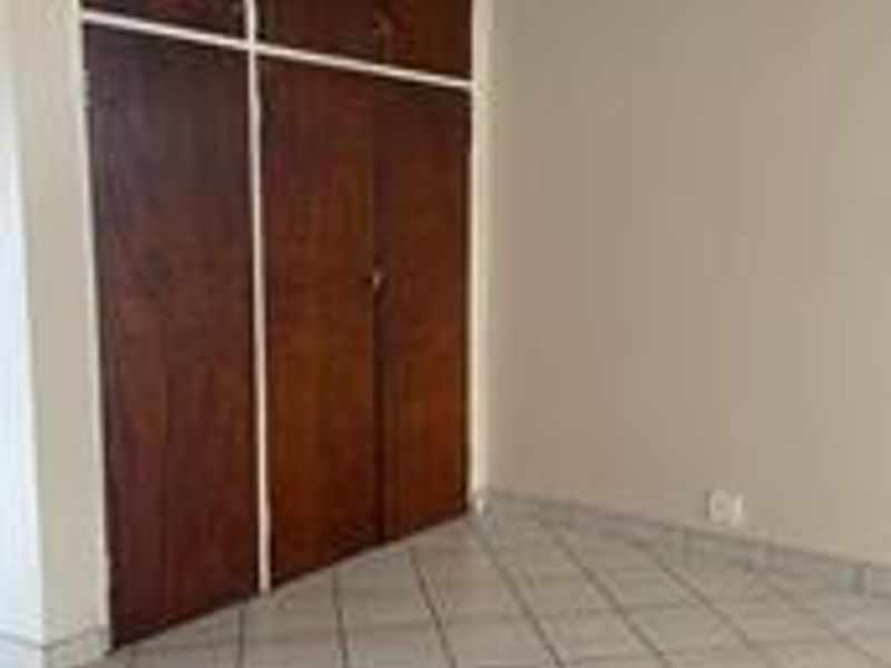 A vacant bedroom featuring tiled flooring and built-in wooden cupboards.
