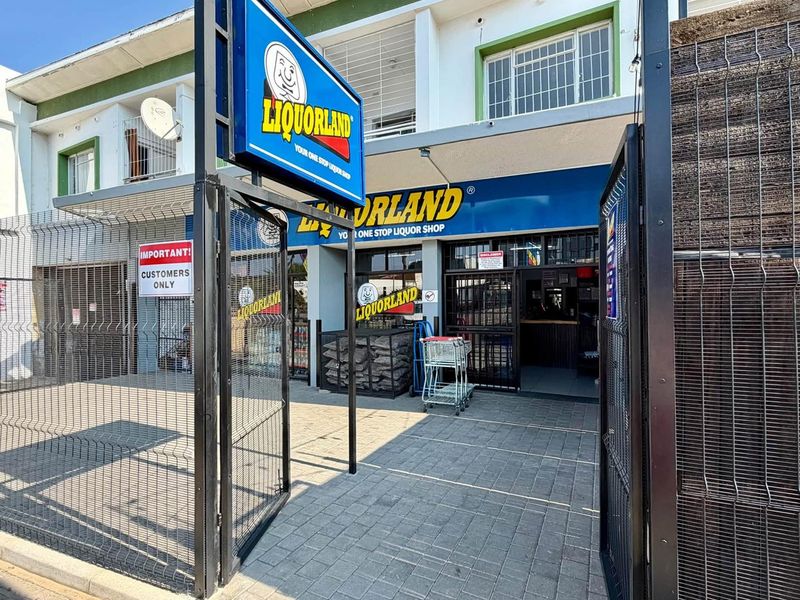 Front exterior view of a commercial retail storefront featuring paved access, security fencing, and prominent branding signage.