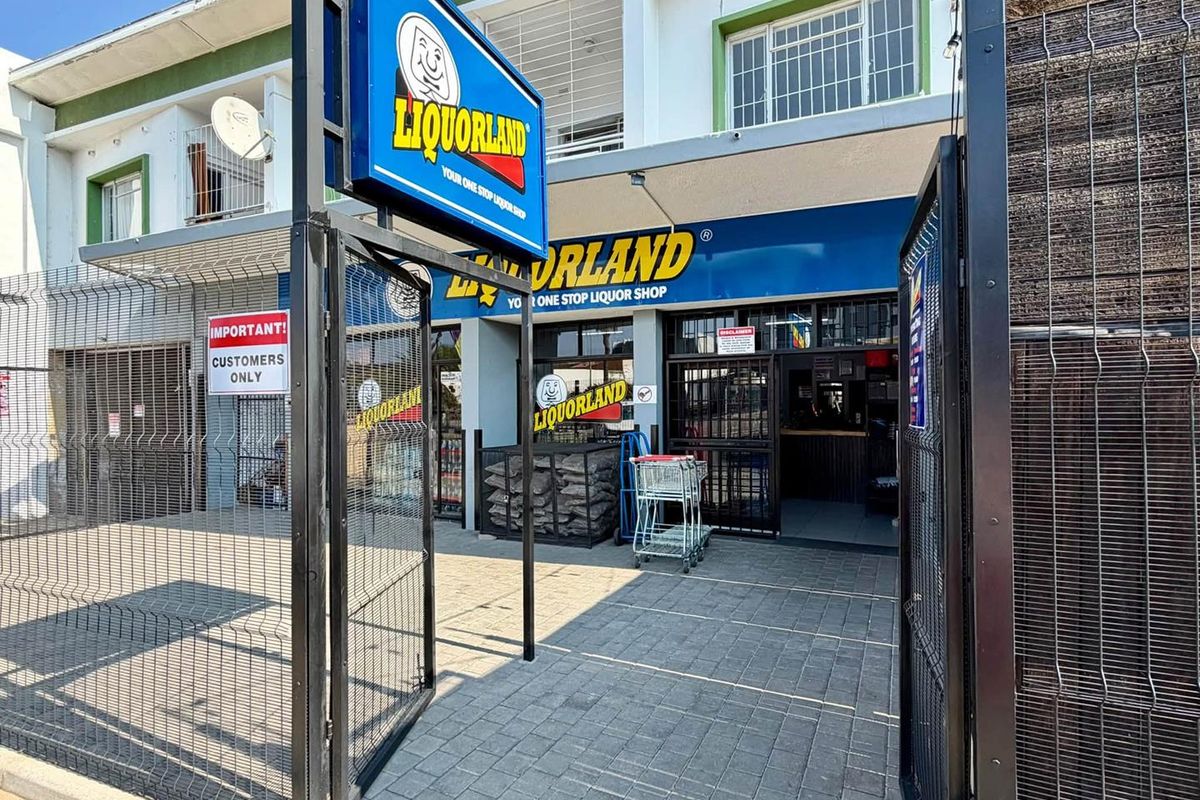 Front exterior view of a commercial retail storefront featuring paved access, security fencing, and prominent branding signage.
