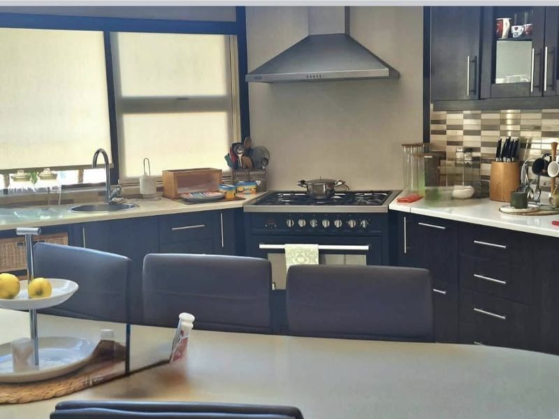 Modern kitchen featuring dark cabinetry, stone countertops, a gas stove with extractor fan, and a tiled backsplash.
