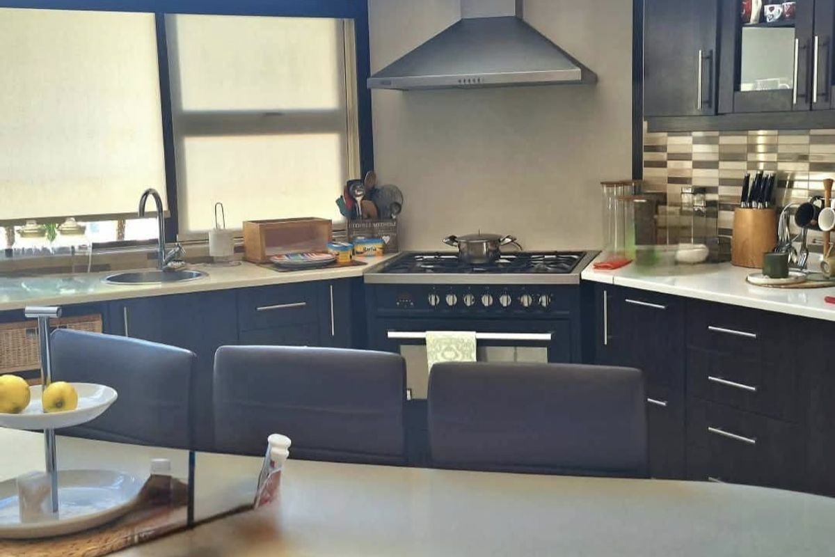 Modern kitchen featuring dark cabinetry, stone countertops, a gas stove with extractor fan, and a tiled backsplash.
