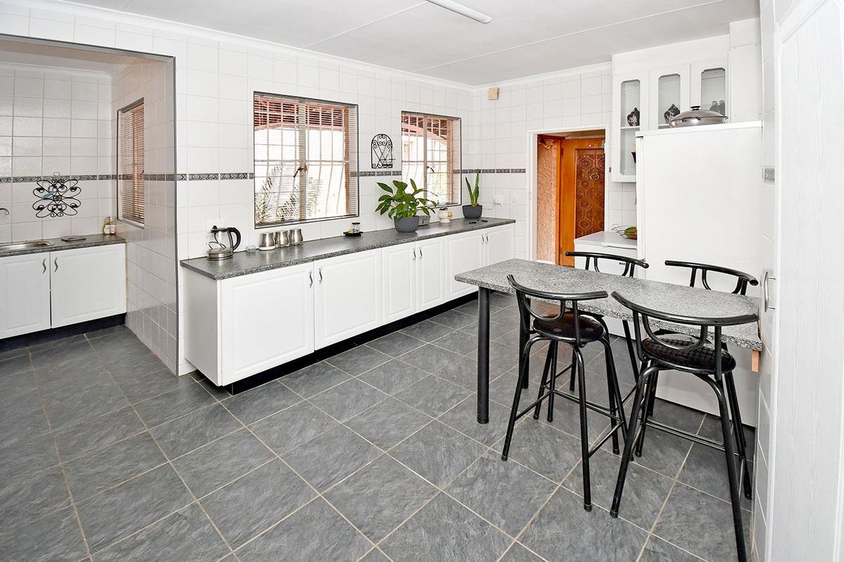 A functional kitchen featuring white cabinetry, granite-look countertops, tiled flooring, and an adjoining scullery area with additional sink and storage space.
