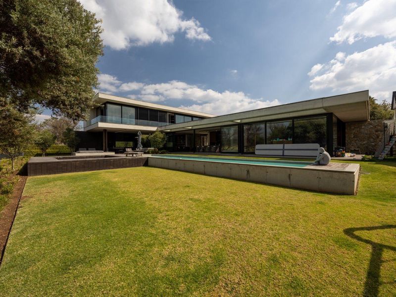 Modern architectural rear elevation featuring a long lap pool, expansive timber and concrete decking, and large sliding glass doors opening to the garden.