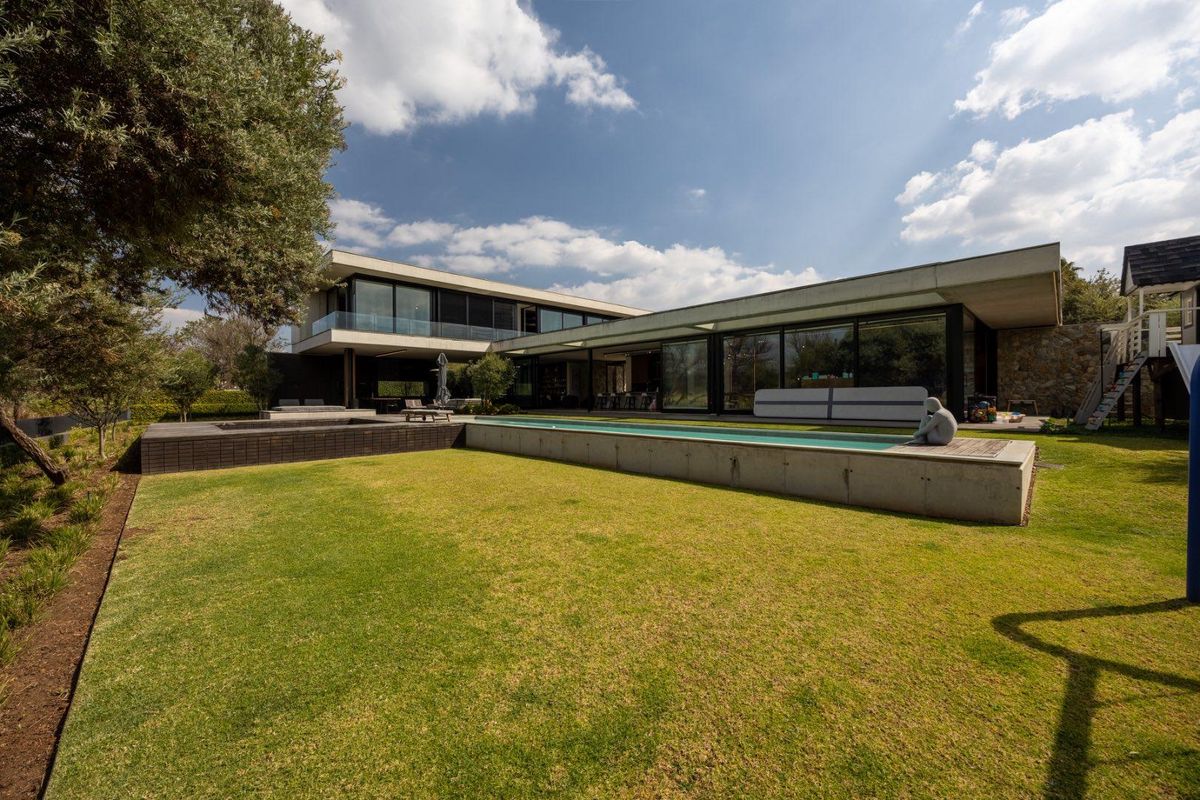 Modern architectural rear elevation featuring a long lap pool, expansive timber and concrete decking, and large sliding glass doors opening to the garden.