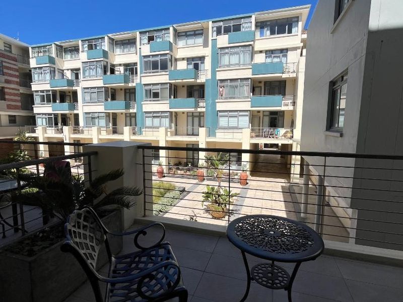 A spacious balcony with tiled flooring and metal balustrades, overlooking the apartment complex courtyard.