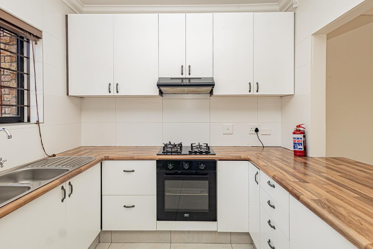 A clean, functional kitchen featuring white cabinetry, wood-look laminate countertops, a gas hob, built-in oven, and a stainless steel double sink.