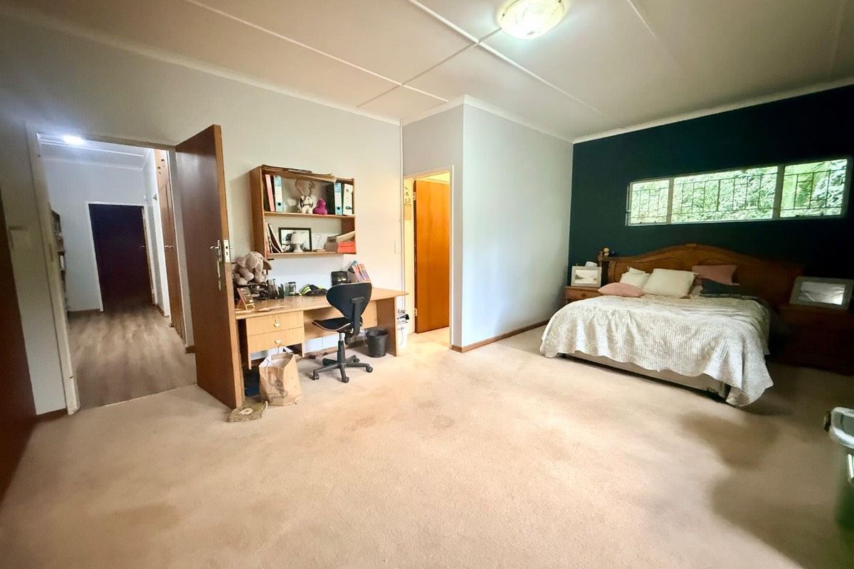 Spacious bedroom featuring neutral carpeting, a dark accent wall, and built-in shelving, providing a functional layout with direct access to the hallway.