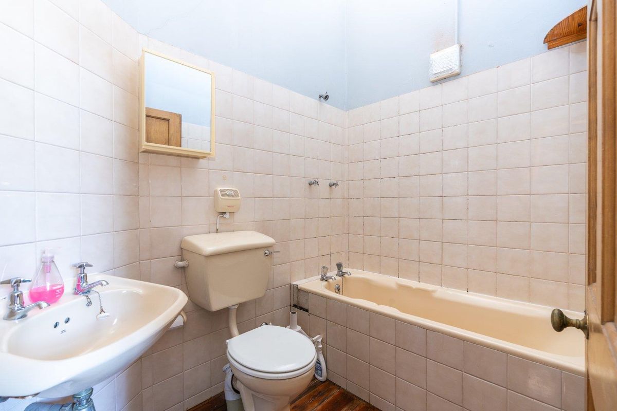 A dated bathroom featuring a bathtub, pedestal sink, and toilet with neutral wall tiling, offering potential for a modern renovation.