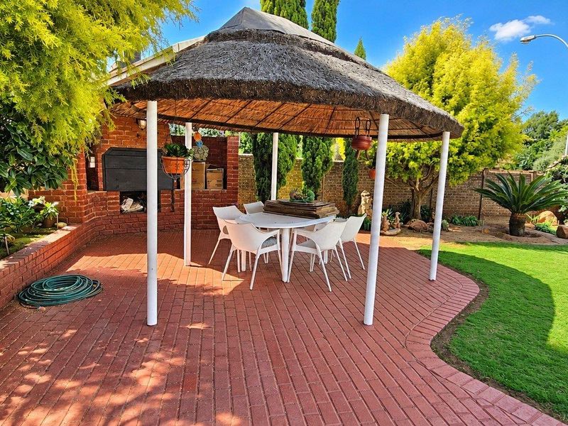 Outdoor entertainment area featuring a thatched lapa, built-in brick braai, and paved patio overlooking a landscaped garden.