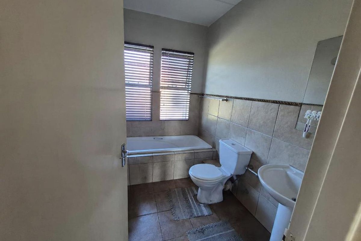 A functional bathroom featuring a built-in bathtub, pedestal sink, and toilet with tiled walls and flooring.