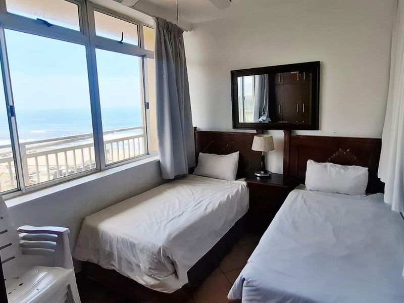 A bedroom featuring large windows with ocean views, tiled flooring, and a built-in headboard, offering a bright and airy atmosphere.