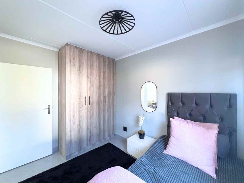 A well-maintained bedroom featuring a built-in wood-finish wardrobe and a modern ceiling light fixture.