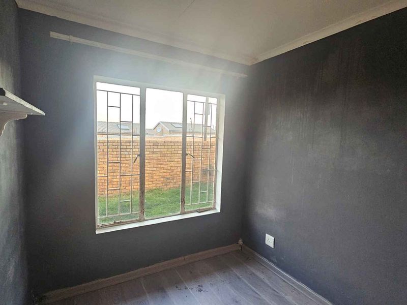 An empty bedroom featuring dark painted walls, laminate flooring, and security bars on the window, offering a blank canvas for renovation.