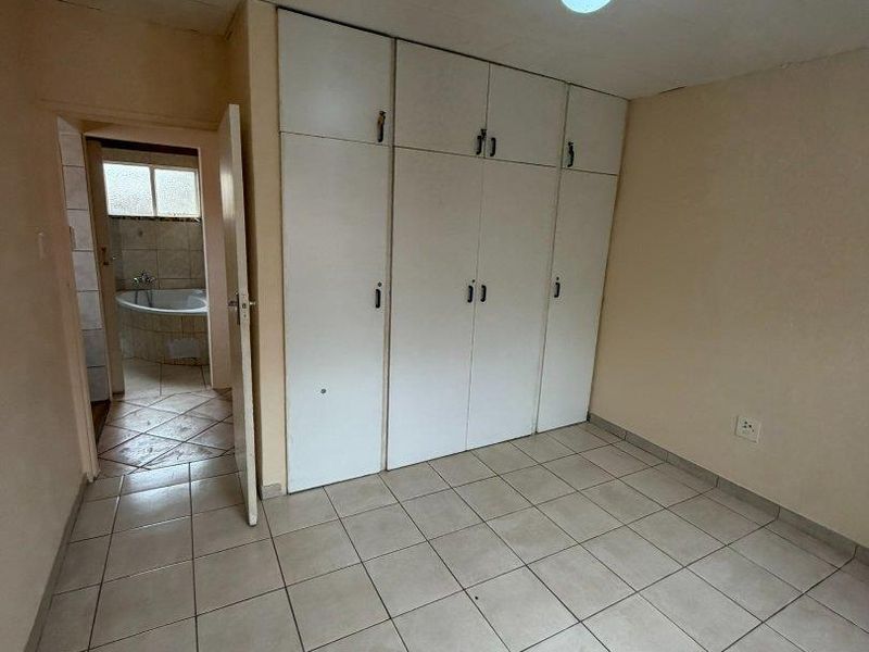 An empty bedroom featuring tiled flooring, built-in cupboards, and direct access to an en-suite bathroom.
