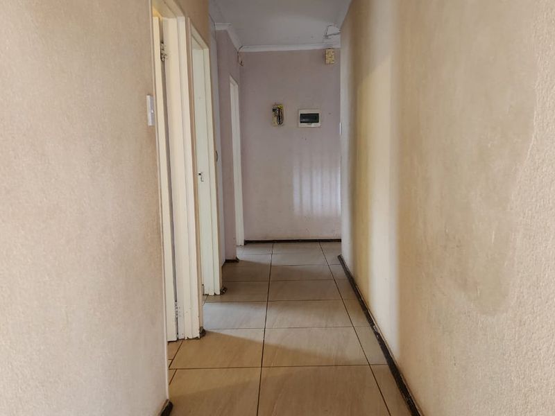 A vacant interior hallway featuring tiled flooring and multiple internal door access points, showing signs of wear on the walls.