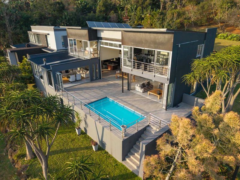 Aerial view of a modern multi-level home featuring a swimming pool, expansive patio, balcony, and solar panels set within a landscaped garden.