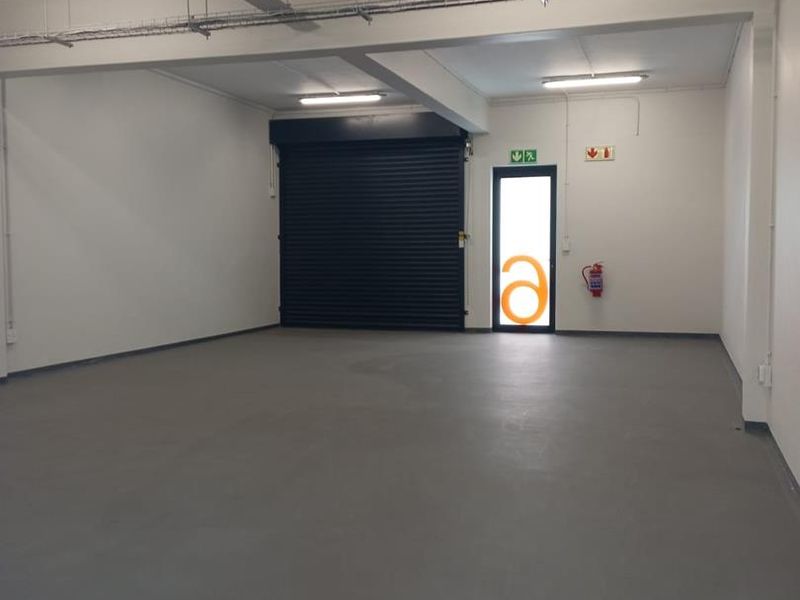 Spacious industrial garage or warehouse unit featuring a roller shutter door, smooth concrete flooring, and functional overhead lighting.