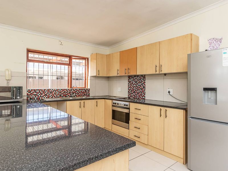 Functional kitchen featuring granite countertops, laminate cabinetry, built-in oven, hob, and tiled splashback with security bars on the window.