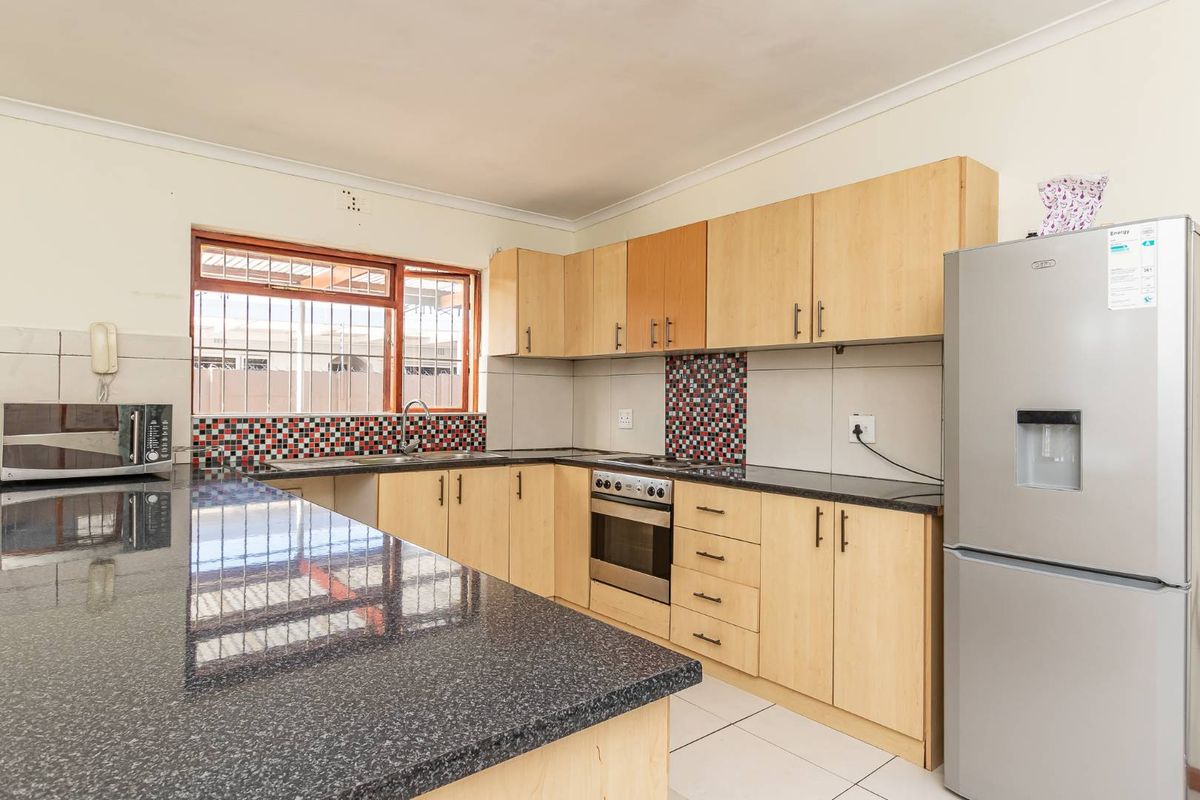 Functional kitchen featuring granite countertops, laminate cabinetry, built-in oven, hob, and tiled splashback with security bars on the window.