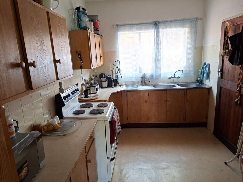 A dated kitchen featuring wooden cabinetry, a double basin sink, tiled splashbacks, and a freestanding electric stove with laminate countertops.