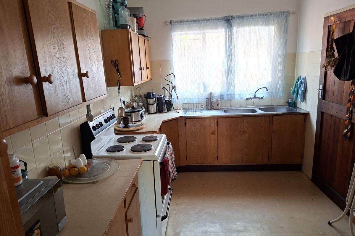 A dated kitchen featuring wooden cabinetry, a double basin sink, tiled splashbacks, and a freestanding electric stove with laminate countertops.