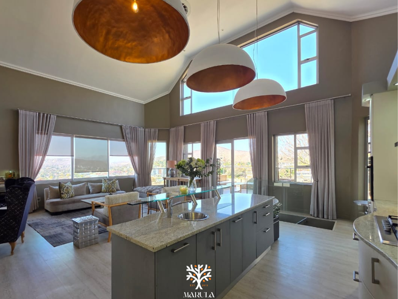 Spacious open-plan living and kitchen area featuring a large island with granite countertops, vaulted ceilings, and expansive windows offering panoramic views.