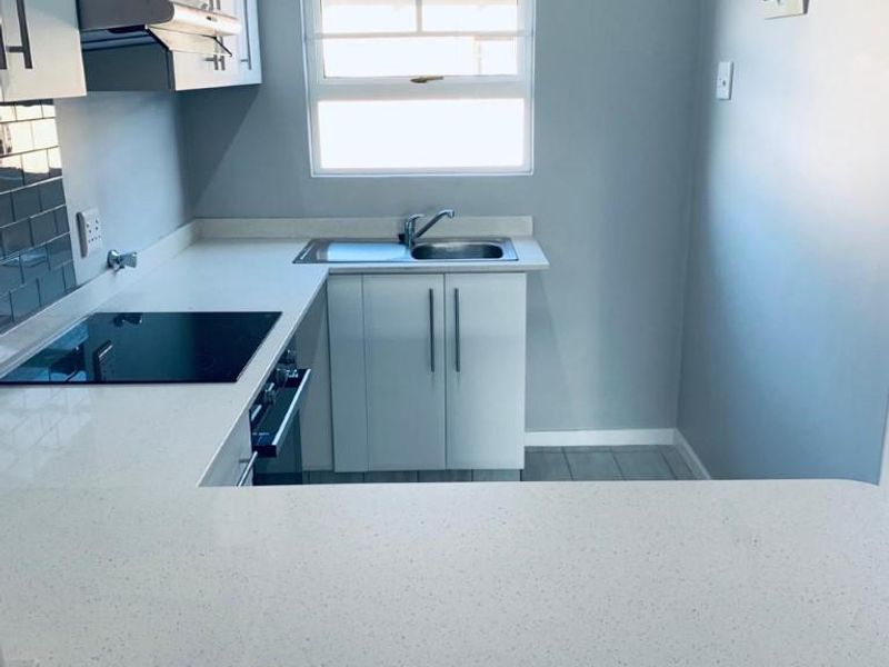 A clean, modern kitchen featuring white cabinetry, stone countertops, integrated appliances, and a tiled backsplash, offering a bright and functional workspace.