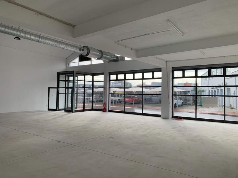 Spacious open-plan retail or commercial unit featuring industrial-style steel-framed windows, exposed ducting, and polished concrete flooring, offering a versatile blank canvas.