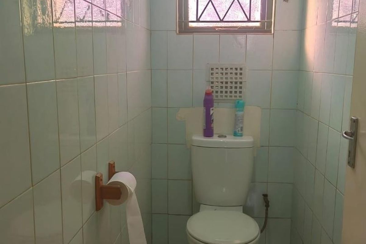 A compact bathroom featuring full-height ceramic wall tiling, a standard toilet, and a window with security bars.
