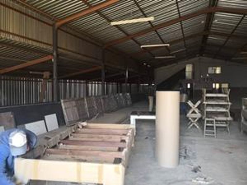 Spacious industrial utility area featuring high corrugated metal ceilings, exposed steel trusses, and durable concrete flooring, suitable for storage or workshop use.