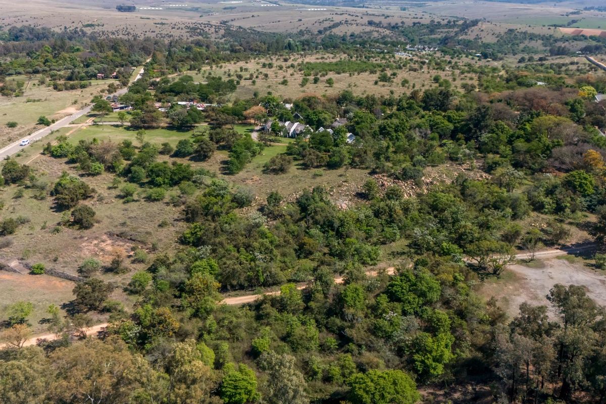 An aerial view of a large small holding property featuring extensive natural vegetation, established trees, and access to both paved and dirt roads.