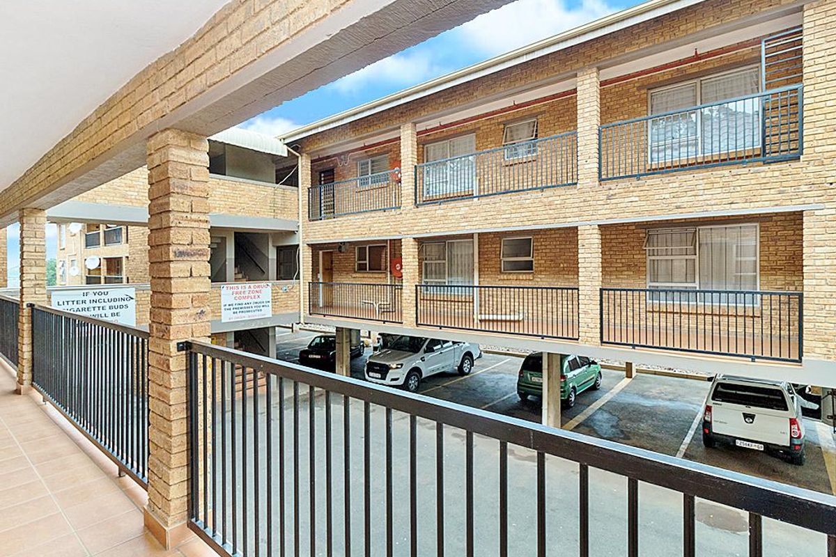 Exterior view of a multi-story townhouse complex featuring brick facade, covered parking bays, and balcony access with metal railings.