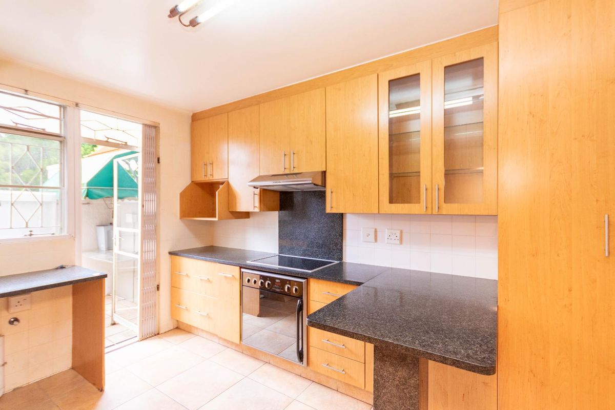 Functional kitchen featuring light wood cabinetry, dark granite countertops, a built-in electric hob and oven, and direct access to an outdoor patio area.