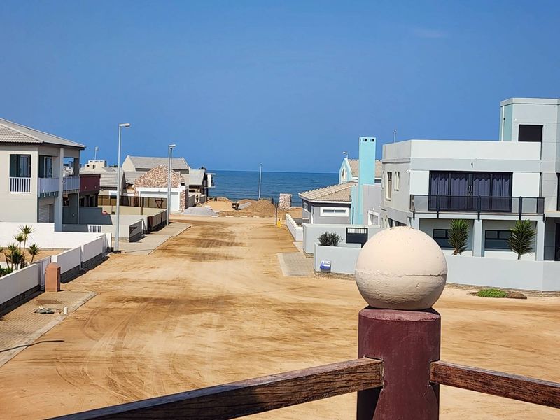 Elevated view overlooking a coastal residential street with sandy road surface and ocean horizon in the distance.