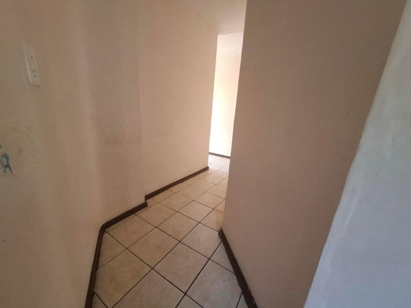 A vacant interior hallway featuring tiled flooring and plain walls, showing signs of wear and requiring cosmetic attention.