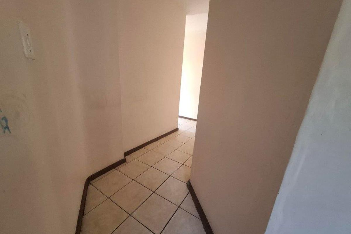 A vacant interior hallway featuring tiled flooring and plain walls, showing signs of wear and requiring cosmetic attention.