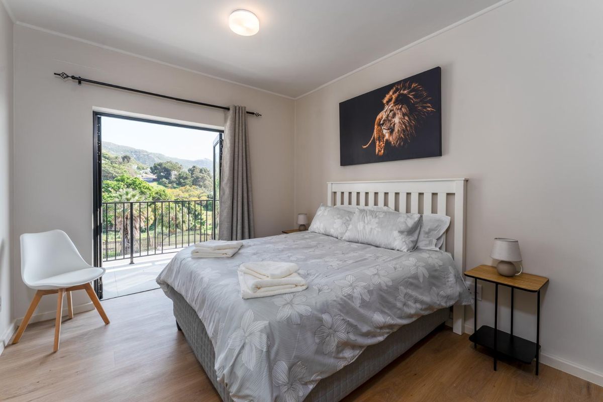 A bright bedroom featuring light wood-look flooring, a built-in curtain rod, and a glass door providing direct access to a private balcony with scenic views.