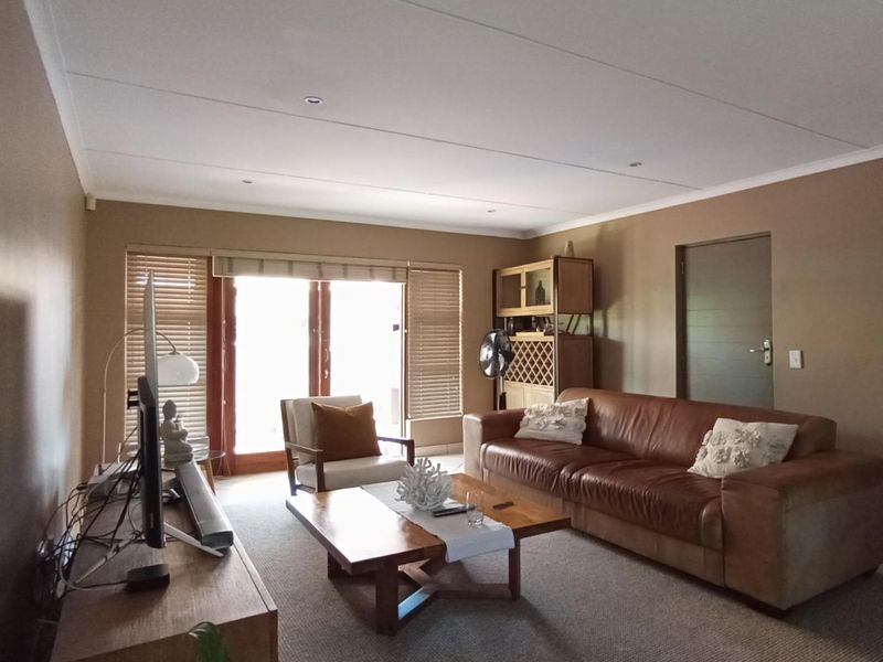 A comfortable living room featuring tiled flooring, recessed downlights, and timber-framed sliding doors that provide access to the outdoor area.