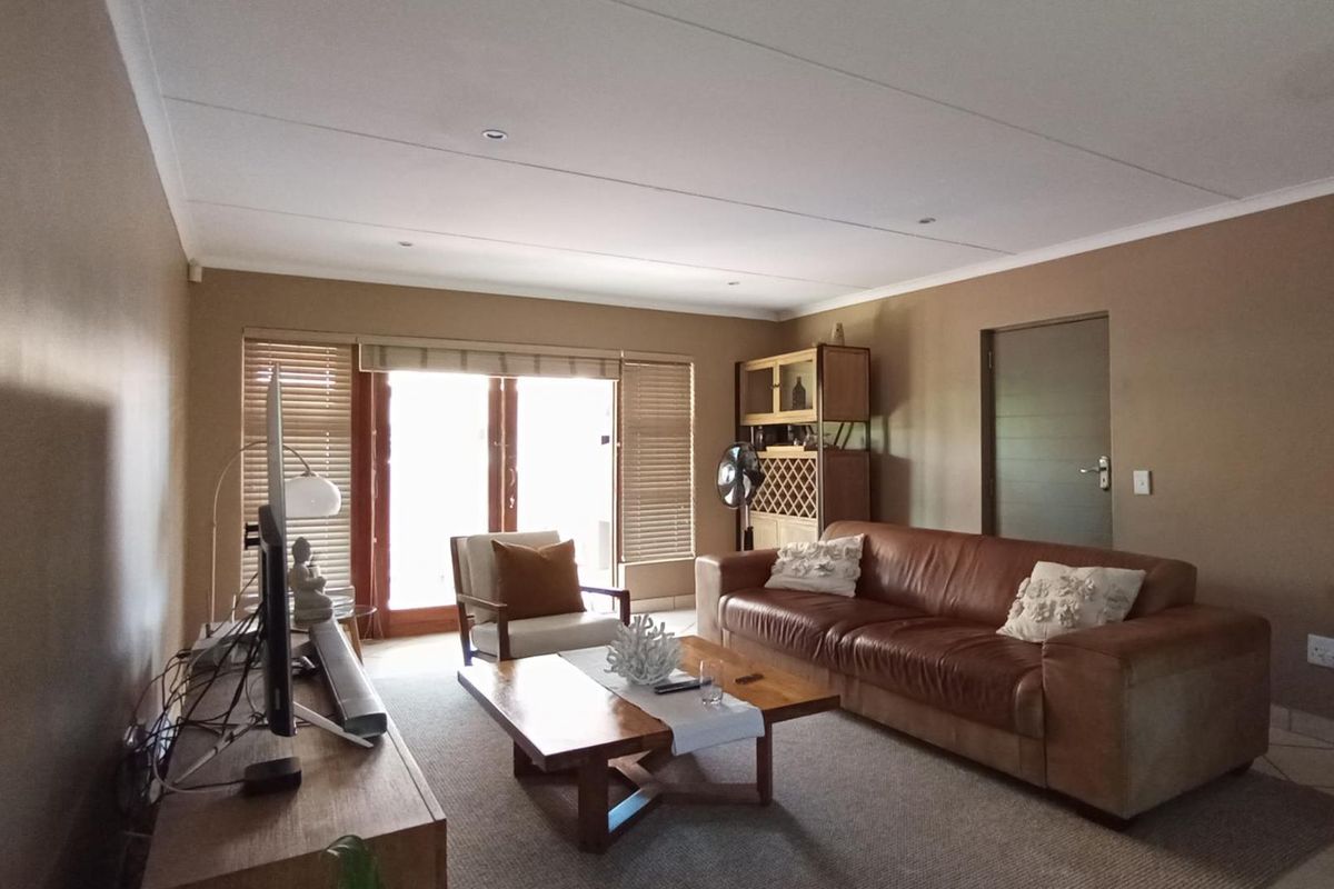 A comfortable living room featuring tiled flooring, recessed downlights, and timber-framed sliding doors that provide access to the outdoor area.